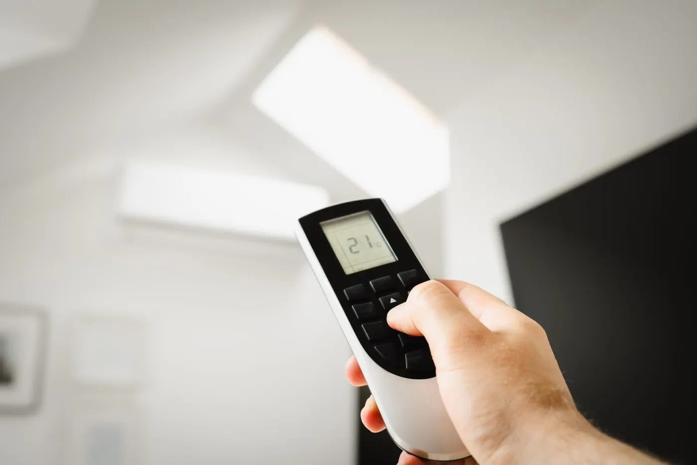 Télécommande de climatisation réversible réglée sur 21 °C, unité murale en arrière-plan